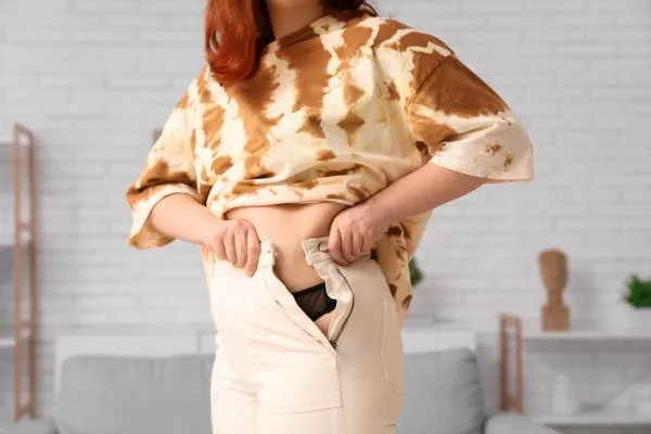 Image of woman trying to do her trousers up after pregnancy weight gain Lewisham