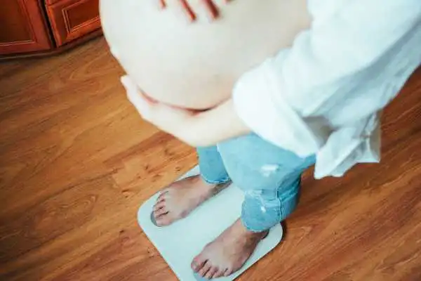 Image of woman weighing herself and experiencing weight gain through pregnancy Lewisham